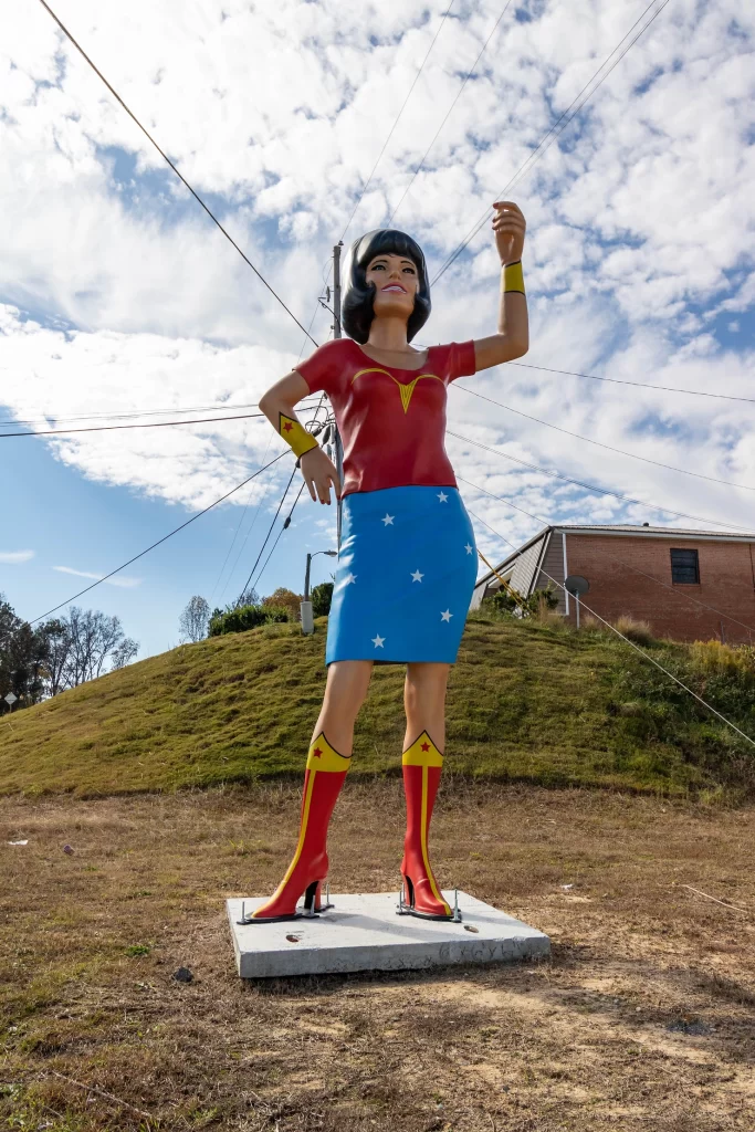 Wonder Woman Roadside Attraction in Dallas Georgia. Large wonder woman sculpture holding her arm up in the air against a blue sky. 
